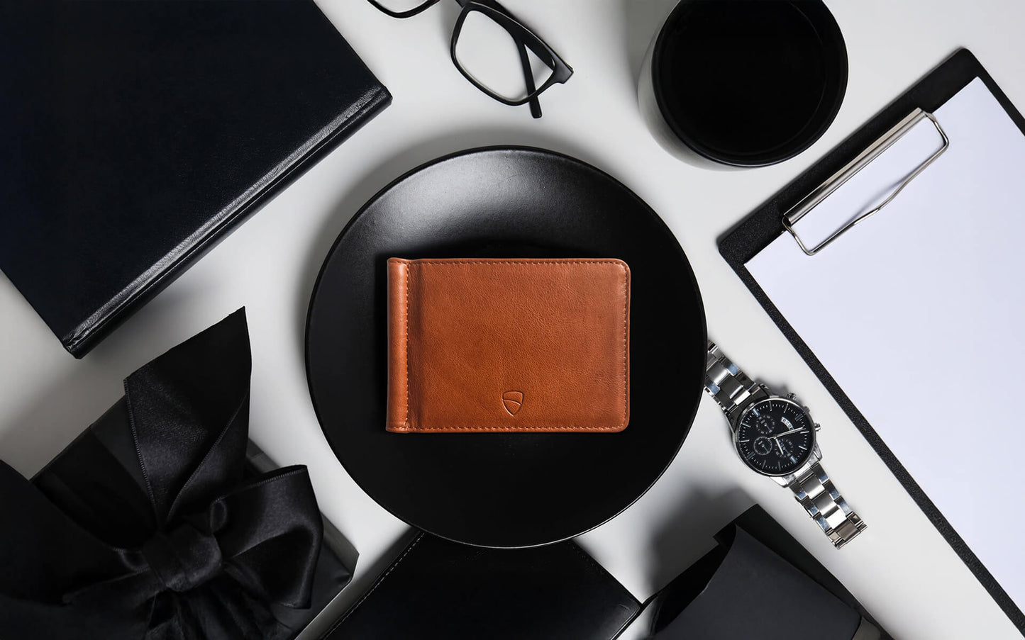 Vaultskin BROMPTON cognac leather wallet on black desk with watch and notebook, luxury slim RFID wallet for men and women